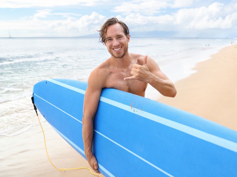 A man is standing with a blue surf on the sandy beach with the ocean behind