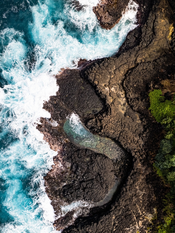 Aerial view of the ocean waves hitting black lava rock.