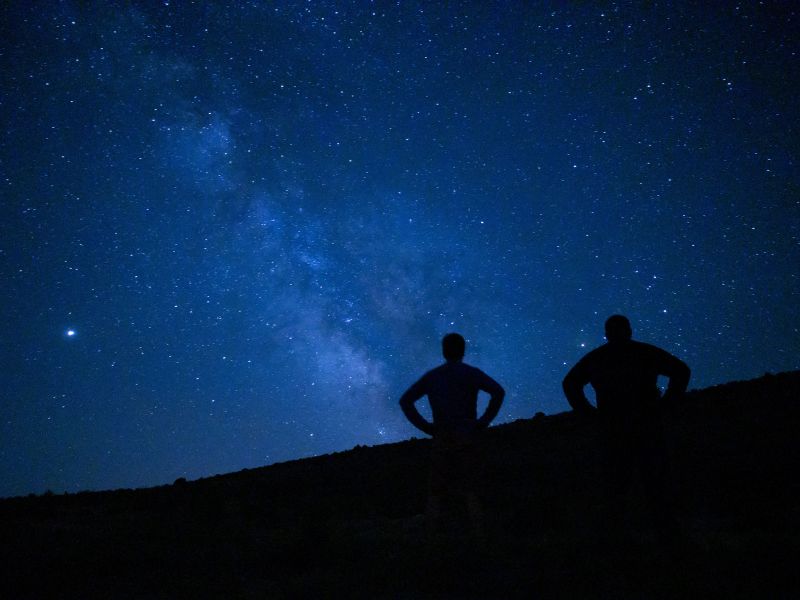Two dark silhouette on top of a hill overlooking a starry night sky. 