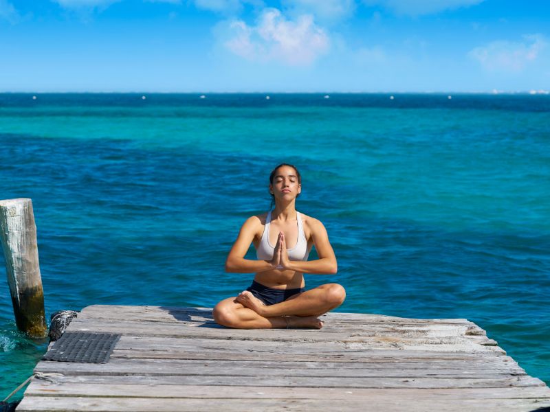 Woman doing a yoga pose at the end of a pier before a blue turquoise ocean. 