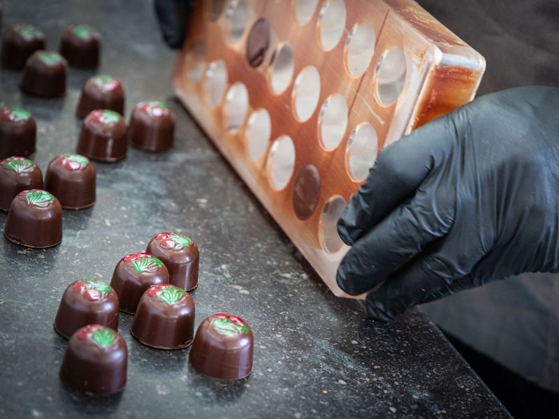 A hand is emptying a bonbon-making form. Ready chocolate bonbons are on a grey counter. 