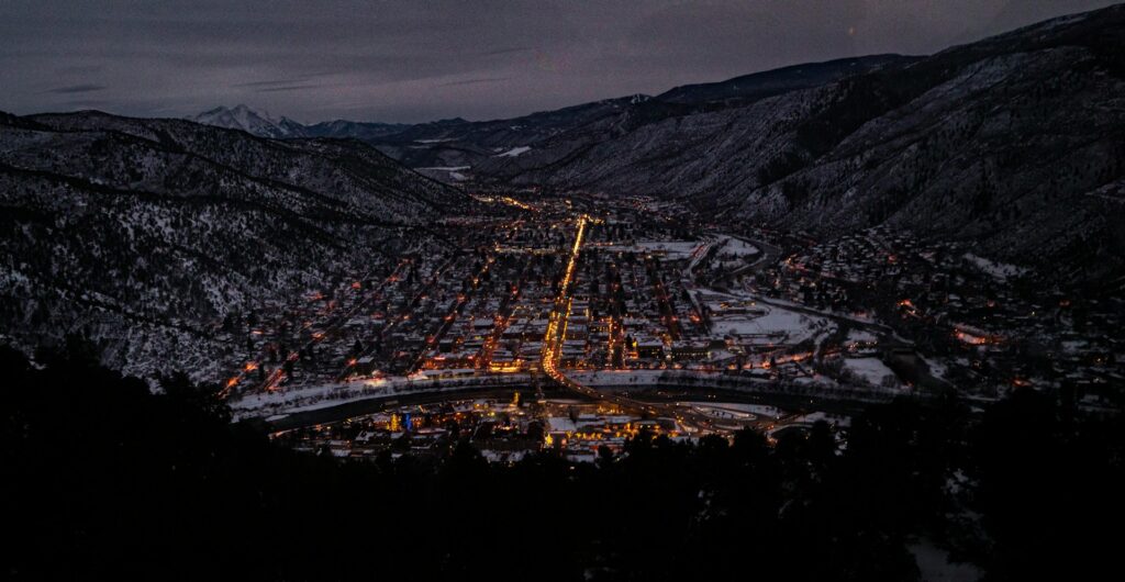 A city in the night with lights on surrounded by mountains. 
