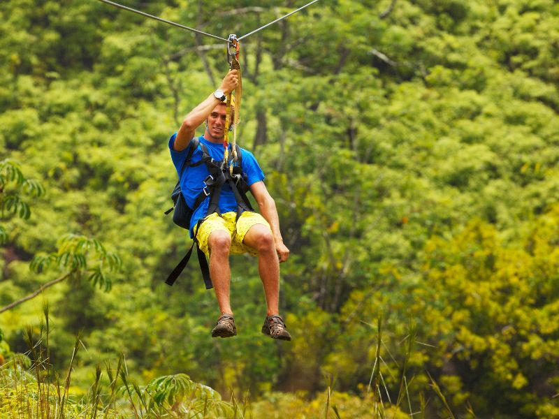 A man is zip lining above the trees