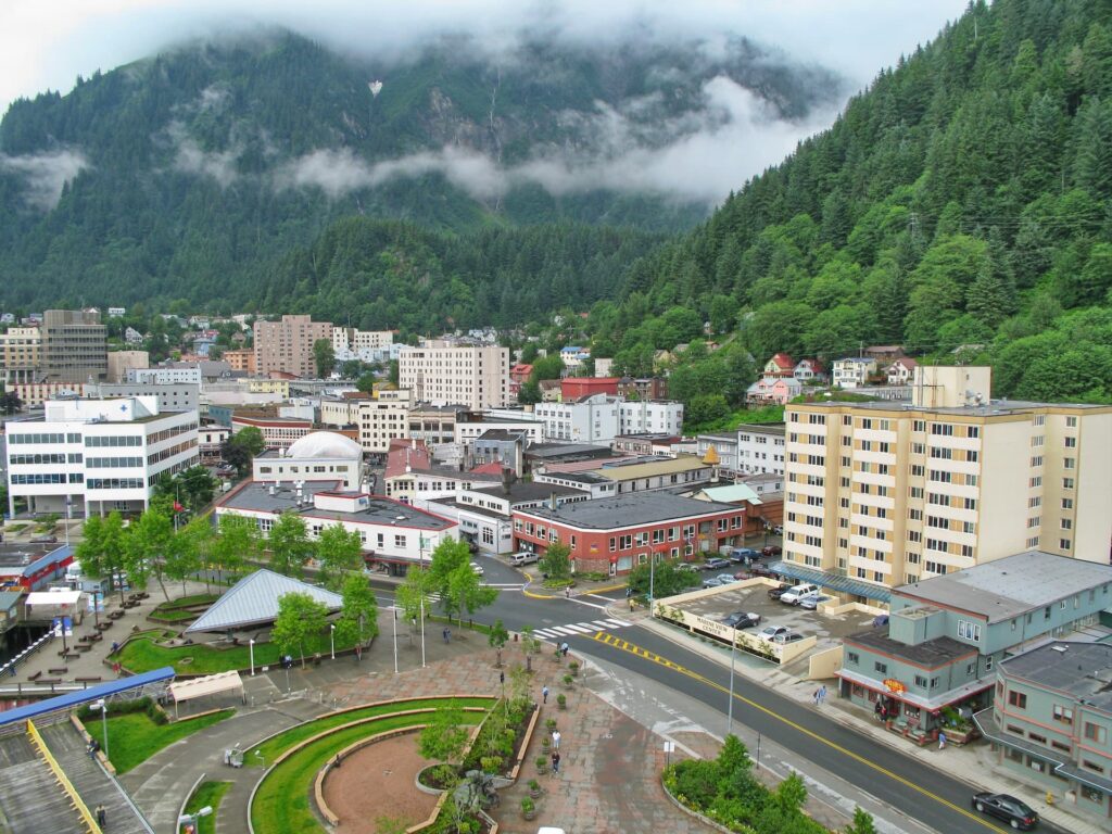 A town with smaller buildings are nested at the foot of a green mountain