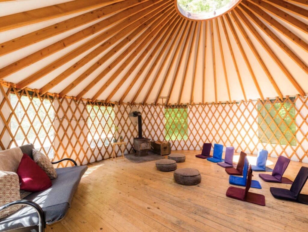 The inside of a yurt with a wood stove, a sofa bed and several pillows to sit on. 