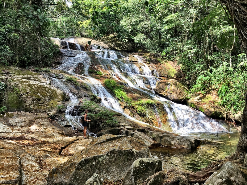 A smooth brown rocky slope with thin water cascading all around it. People are hiking along the sides.