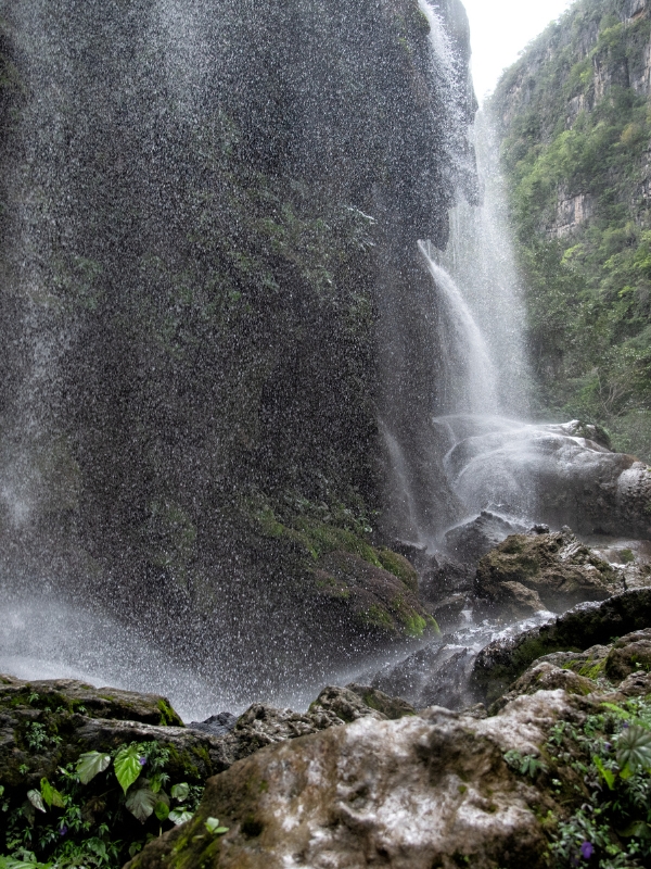 A mist of a waterfall in front of moss-covered brown cliff.