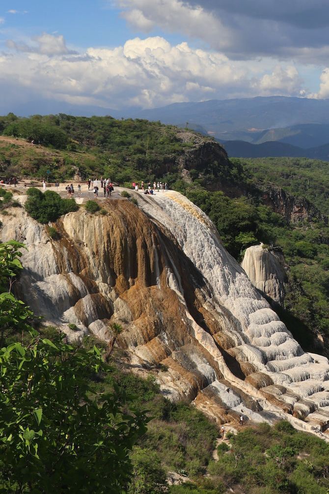 A waterfall is flowing through a white and brown limestone formation.