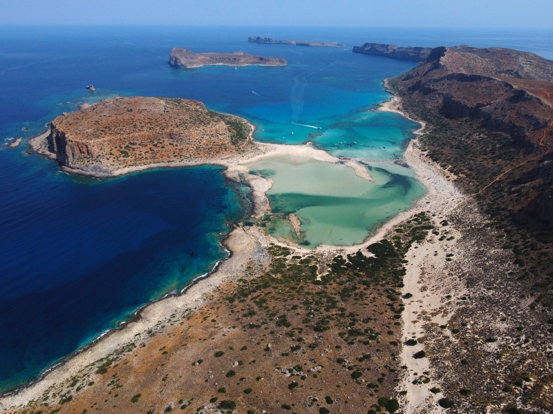 A lagoon from above surrounded by rock and sandy shores.