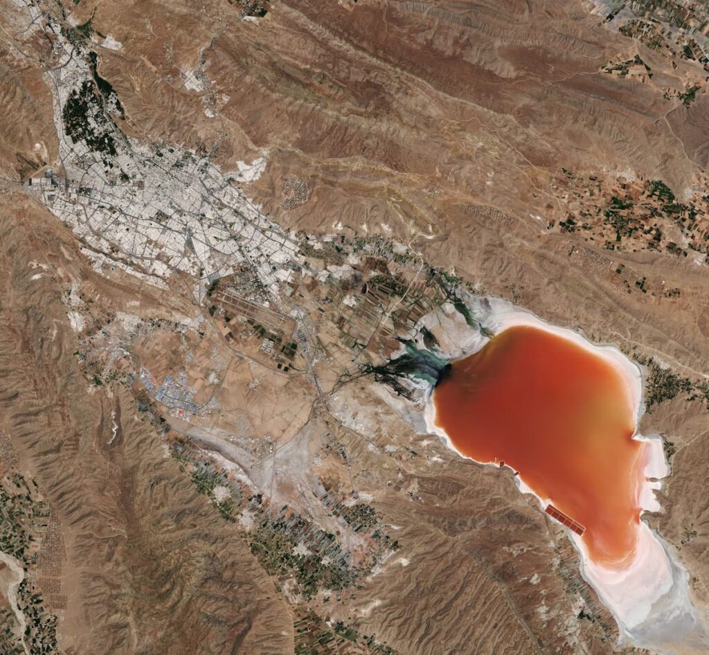 Ariel photo of a red lake surrounded by brown terraine. 