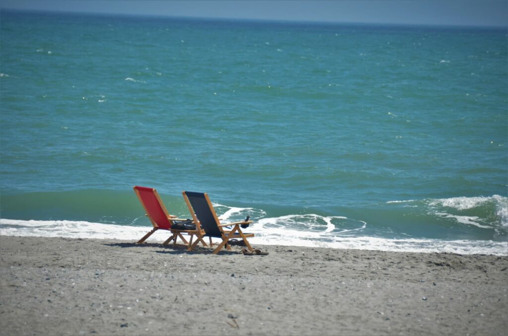 Sandy beach with two empty adirondack chairs. 