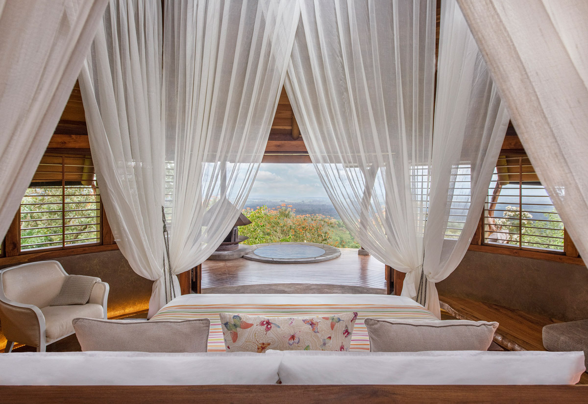 Double bed with white mosquito net overlooking an open door and vistas. 