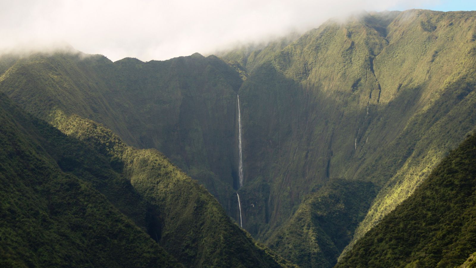 Large mountains covered with green vegetation and a tall waterfall cascading in the middle. 