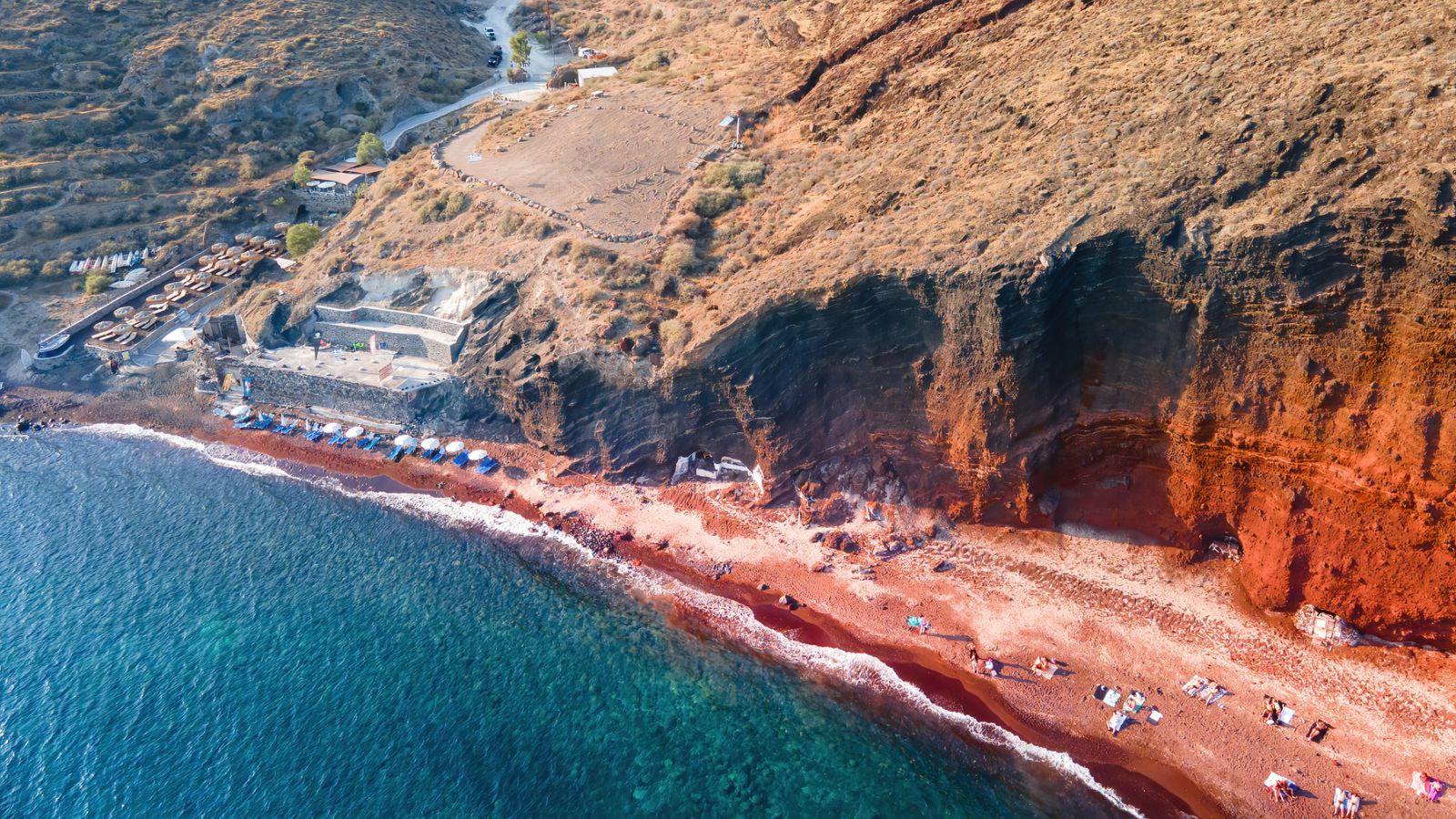 huge red cliff with a narrow red sand beach