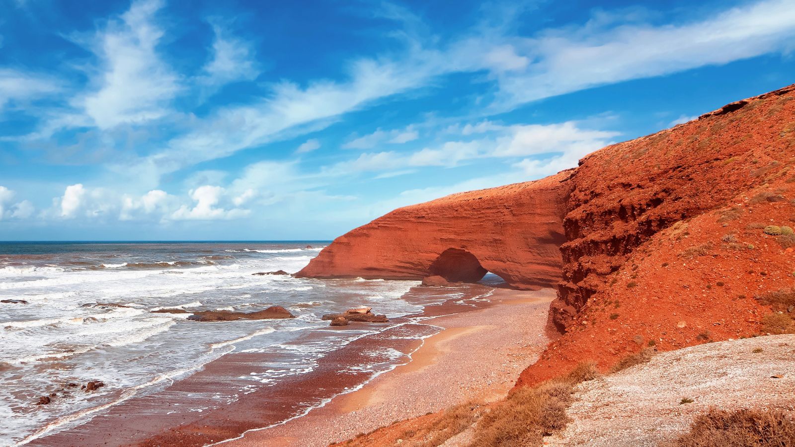 Red-orange cliffs along a red sand shore.