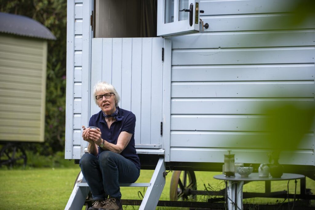 A woman is sitting in front of a light blue shepherd's hut.